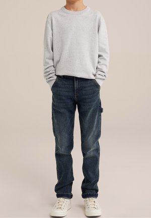 Jasnoszara bluzka z dekoltem okrągłym w kolorowe plamki, niebieskie dżinsy z bocznymi kieszeniami i białe trampki. Luźny krój z ściągaczami przy mankietach i w pasie.