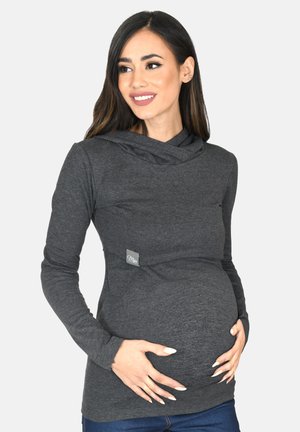 Dunkelgraues langärmeliges Umstandstop mit Wasserfallausschnitt, weicher Textur und einem kleinen Markenschild vorne, tailliert gefertigt, um einen wachsenden Babybauch zu umschließen.
