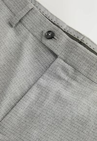 Grau gemusterte Hose mit strukturierter Webung, ausgestattet mit einem schwarzen Knopf und gesteppten Details an der Taille. Nahaufnahme des Stoffes und Designs.