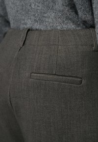 Pantaloni gri cu model în colțar, croi slim, cu buzunar în spate și talie structurată. Materialul are un finisaj neted, texturat.