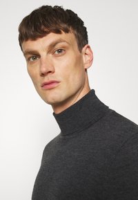 Pull en laine gris foncé avec un design ajusté, un col et des poignets côtelés, fabriqué en matériau tricoté doux, au style minimaliste et sans motifs.