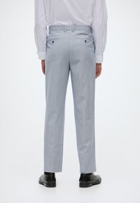 Ανοιχτοί γκρι παντελόνια με διακριτό καρό σχέδιο, επίπεδο μπροστινό μέρος, δύο πίσω τσέπες και ευθεία γραμμή, σε συνδυασμό με μαύρα επίσημα παπούτσια.