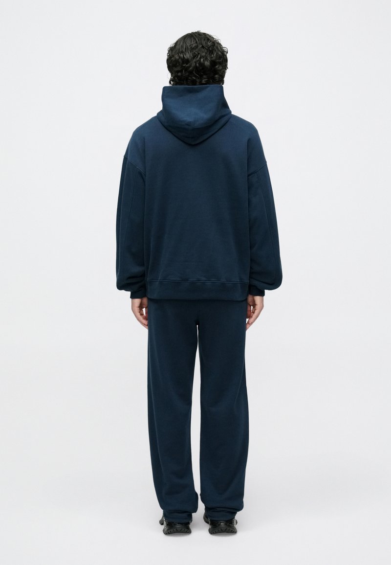 Navy blue hoodie and sweatpants in soft fabric. Loose fit with a large hood and ribbed cuffs. Minimalistic design without visible logos.