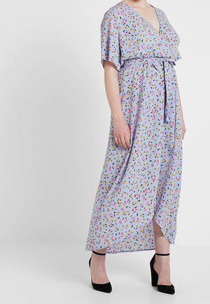 Kvinde iført en lyseblå floral slå-om-kjole med korte ærmer, taljebånd og frontslids, kombineret med sorte ankelsnørestiletter.