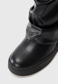 Botte en cuir noir à la cheville avec une texture lisse, un bout rond et un dessus arrondi. Dispose d'une semelle en caoutchouc épaisse pour un soutien supplémentaire.