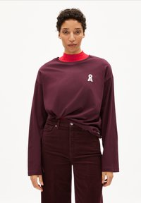 Bordeaux lange mouwen t-shirt met een ronde hals en een wit lintlogo op de borst, gecombineerd met donkerbordeaux corduroy broek.
