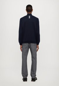Felpa navy con colletto alto e righe bianche orizzontali sul retro. Abbinata a jeans di jeans grigi e scarpe nere.