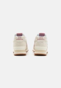 Baskets en daim beige avec un dessus en mesh blanc, présentant un onglet de talon bordeaux et le logo "new balance" à l'arrière. Semelle en caoutchouc.