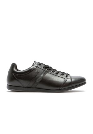Baskets en cuir noir avec une texture lisse, bout rond, fermeture à lacets et accent latéral subtil. Dotées d'une semelle en caoutchouc à profil bas.