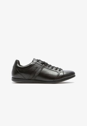 Zapatillas negras de cuero con textura suave, punta redonda, cierre de cordones y sutil acento lateral. Presenta una suela de goma de perfil bajo.