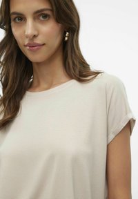 Camicetta corta a maniche corte beige chiaro con una texture a coste e un collo rotondo. Il tessuto appare morbido e traspirante.