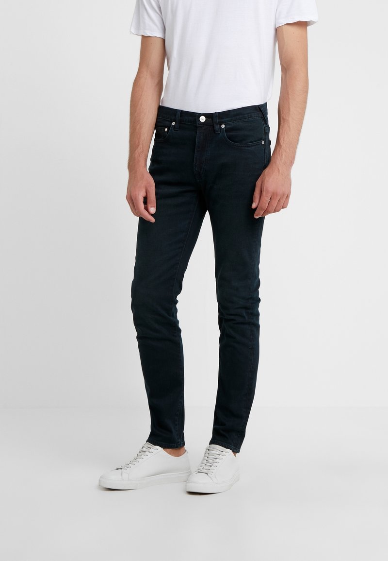 Dark blue jeans made of denim, featuring a slim fit and five-pocket design, paired with white sneakers and a plain white t-shirt.