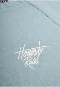 Vaaleansinisessä collegepaidassa on ribbikuvio ja edessä on brodeerattu valkoinen teksti "Honesty Rules". Pyöreä pääntie ja raglan-hihat.