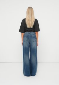 Lichtblauwe wijdvallende jeans met een vervaagde textuur, van denimmateriaal, vijf zakken en een hoog tailledesign, gecombineerd met een zwarte top met korte mouwen.