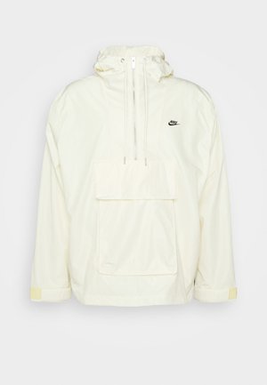 Weißer Nylon-Anorak mit Kapuze, Fronttasche, verstellbaren Kordeln und gelben Akzenten an den Bündchen; zeigt ein kleines schwarzes Logo.