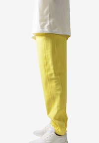 Pantaloni de jogging galbeni dintr-un material moale, cu un fit slim, manșete elastice și cusături laterale contrastante, asortați cu adidași albi.