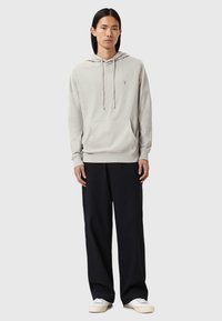 Haut de hoodie gris clair avec une poche avant et des cordons, associé à un pantalon noir ample et des baskets blanches. Texture lisse, design minimal.