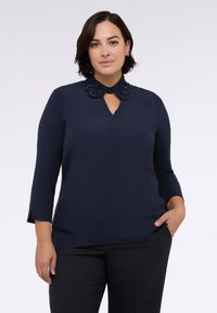Blusa navy con scollo a chiave e colletto testurizzato decorato con perline. Caratterizzata da maniche a tre quarti e una vestibilità rilassata.