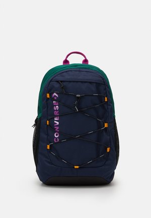 Navy and green backpack with front elastic cord, purple "Converse" logo, side mesh pockets, and a pink top handle.
