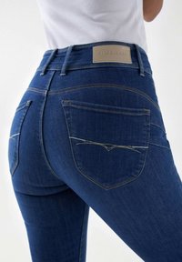 Jeans de mezclilla azul oscuro con cintura alta, que cuentan con costuras en contraste, dos bolsillos traseros y un parche de cuero con el logo.