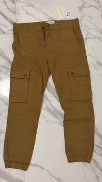 Pantaloni cargo beige realizzati in un tessuto dalla superficie liscia, dotati di due tasche cargo laterali, polsini elasticizzati e chiusura frontale con bottone.