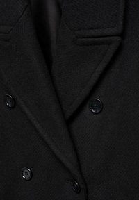 Cappotto nero doppiopetto con tessuto testurizzato, revers a punta e bottoni neri. L'interno ha una finitura liscia.