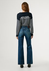 Marineblauwe en witte gestreepte trui met tekstdetails; gecombineerd met blauwe wijde jeans. Zichtbare achterzakken en een lichte slijtage op de jeans.