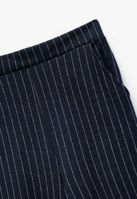 Marineblauwe broek met witte verticale streepjes en zijzak, weergegeven in close-up op een witte achtergrond.