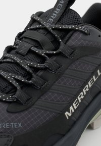 Black hiking shoe featuring a textured mesh upper, reflective laces, and a rubber sole with a patterned finish. Brand name displayed.