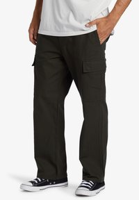 Cargo pants in dark olive green, featuring multiple side pockets, durable material, straight-leg design, and a comfortable fit. Black sneakers visible.