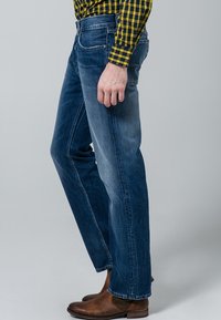 Jeans de mezclilla azul ajustados con un ligero desgastado, cinco bolsillos y un diseño clásico de pierna recta, combinados con botas de tobillo marrones.