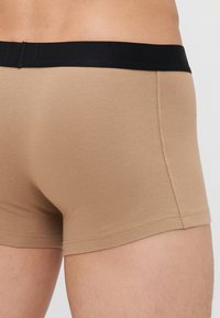 Krémszínű boxeralsó, puha, rugalmas anyagból, fekete elasztikus derékpánttal, szoros illeszkedéssel és diszkrét varrási részletekkel.