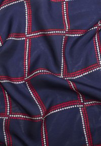 Tissu bleu marine avec un motif à carreaux, présentant des lignes pointillées rouges et blanches qui s'entrecroisent, créant un aspect texturé et superposé.