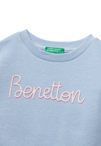 Světle modrá mikina s kulatým výstřihem s výšivkou "Benetton" v bílé a růžové barvě, se zelenou nášivkou "United Colors of Benetton" uvnitř límečku.
