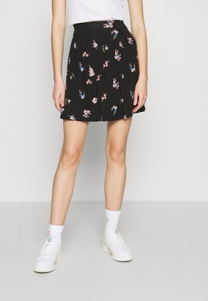 Sort blomsteret nederdel med plisseret design og mønster af lyserøde og blå blomster. Båret sammen med hvide sneakers og hvide ankelsokker.