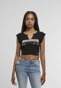 Top corto negro con escote en V y mangas de capucha, con texto en blanco. Combinado con jeans de un azul claro, que presentan un diseño ajustado.