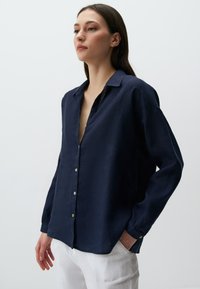 Camicia in lino blu navy con vestibilità rilassata, maniche lunghe e colletto leggermente aperto. Presenta bottoni bianchi e una finitura testurizzata.