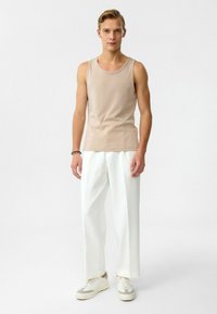 Beige mouwloze tanktop gecombineerd met witte plooibroek en witte sneakers. Glad stof met een aansluitend ontwerp en relaxed fit.