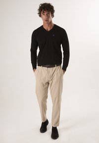 Zwarte lange mouwen V-hals shirt, beige op maat gemaakte broek en zwarte enkellaarsjes. Opvallende details zijn een klein paars logo op het shirt.