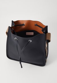 Borsa a secchiello in pelle nera con interni marroni. Caratterizzata da chiusura con coulisse, occhielli in metallo e un dettaglio di branding laterale. Texture liscia.