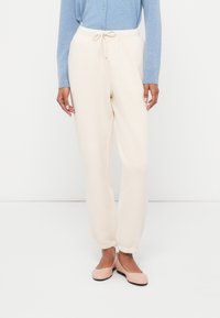 Krémovo sfarbené tepláky s úzkym strihom, šnúrkou v páse a manžetami na koncoch nohavíc, skombinované s svetlomodrým kardigánom s dlhým rukávom.