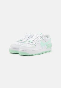 Vita sneakers med mintgröna detaljer, texturerad gummisula, perforerad tå och en märkespanel på sidan. Snörning med vadderad plös.