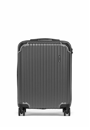 Ciężka walizka o twardej powłoce w ciemnoszarym kolorze z pionowymi żebrowaniami, górnym uchwytem i czterema obrotowymi kółkami, stojąca pionowo na białym tle.
