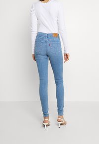 Jeans skinny de mezclilla azul claro con cintura alta, que cuentan con bolsillos traseros y una etiqueta de cuero con la marca. Combinados con una blusa de manga larga blanca.