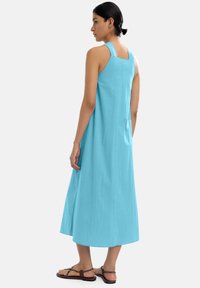 Sukienka bez rękawów o średniej długości w jasnoniebieskim kolorze, z kwadratowym dekoltem i luźnym krojem, zestawiona z brązowymi płaskimi sandałami.