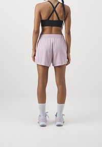 Svart sportbh med korsettsnören, ljuslila shorts med texturerad tyg, vita strumpor och pastellfärgade träningsskor.