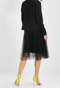 Czarna dopasowana marynarka na czarnej tiulowej spódnicy z ozdobami z koralików, w połączeniu z jas yellow żółtymi sandałami na obcasie.