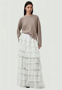 Beige strikket sweater med ribbede manchetter, parret med en hvid lagdelt blonde-maxiskirt med bølgeformede mønstre og lagdelt tekstur.
