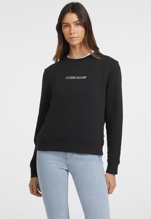 Zwarte sweatshirt van zachte stof, met lange mouwen en een ronde halslijn. "GUESS JEANS" geborduurd in het wit over de borst.