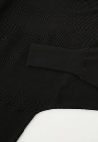 Czarna prążkowana tkanina o gładkiej fakturze, z charakterystycznym detalem rękawów. Kształt jest lekko oversize z luźnym krojem.